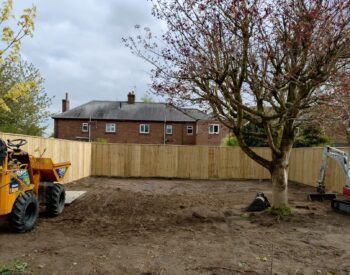 Landscaped garden featuring porcelain paving, paths, a patio with pergola, lush turf, and wooden fencing.