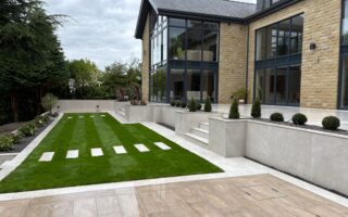 Landscaped hillside garden with terraced patios, lush lawn, and porcelain paving